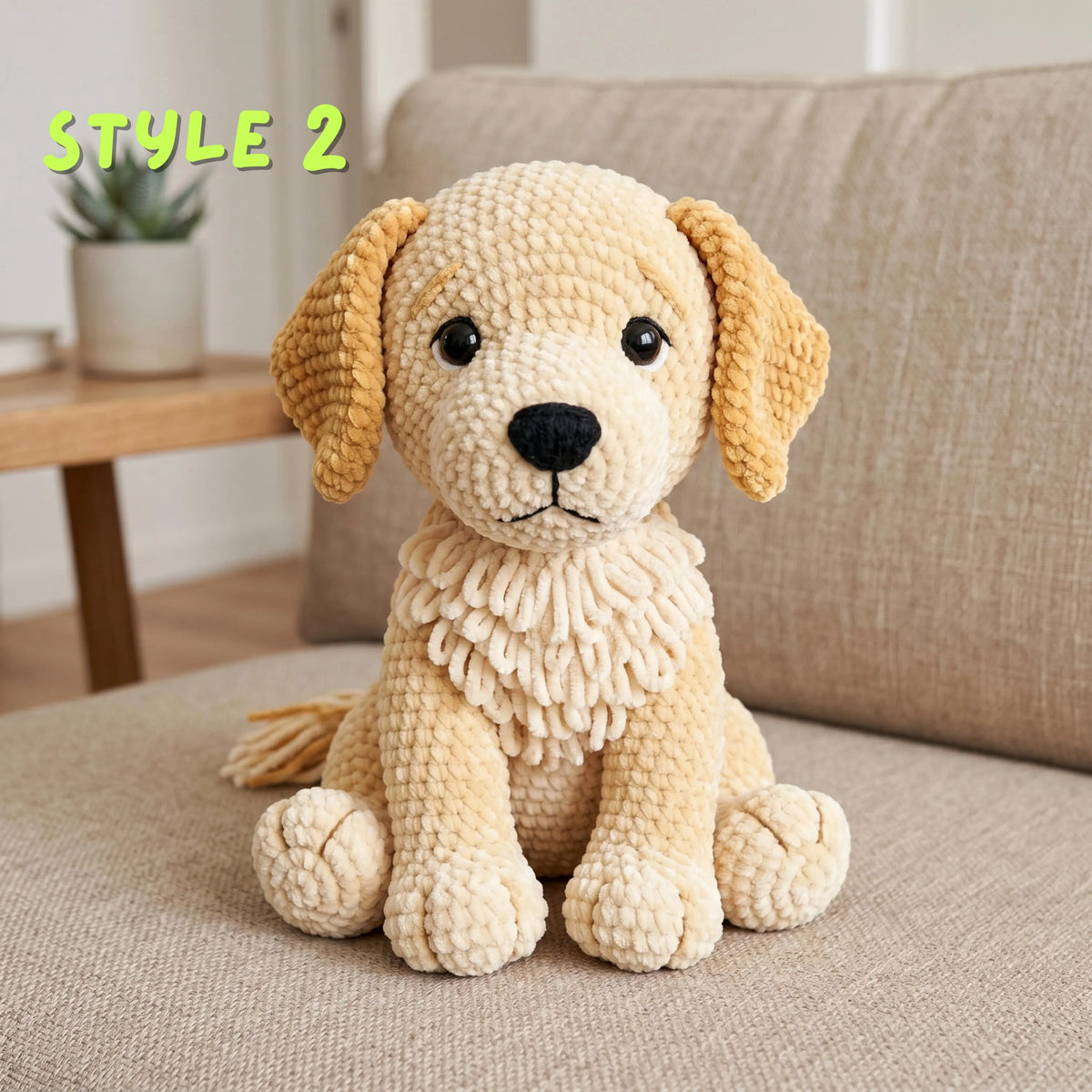 A crocheted plush puppy toy in cream and tan sits on a beige sofa. The dog has floppy ears, black eyes, a black nose, and a textured ruffled collar.