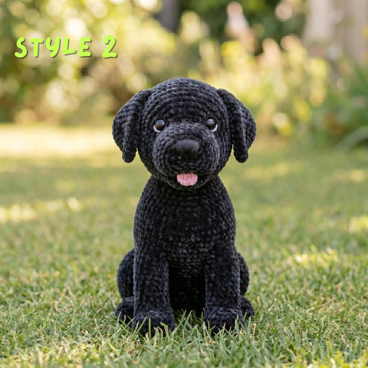 A black crocheted dog toy sits on green grass outdoors with a blurred garden background. The text 'STYLE 2' appears in the top left corner.