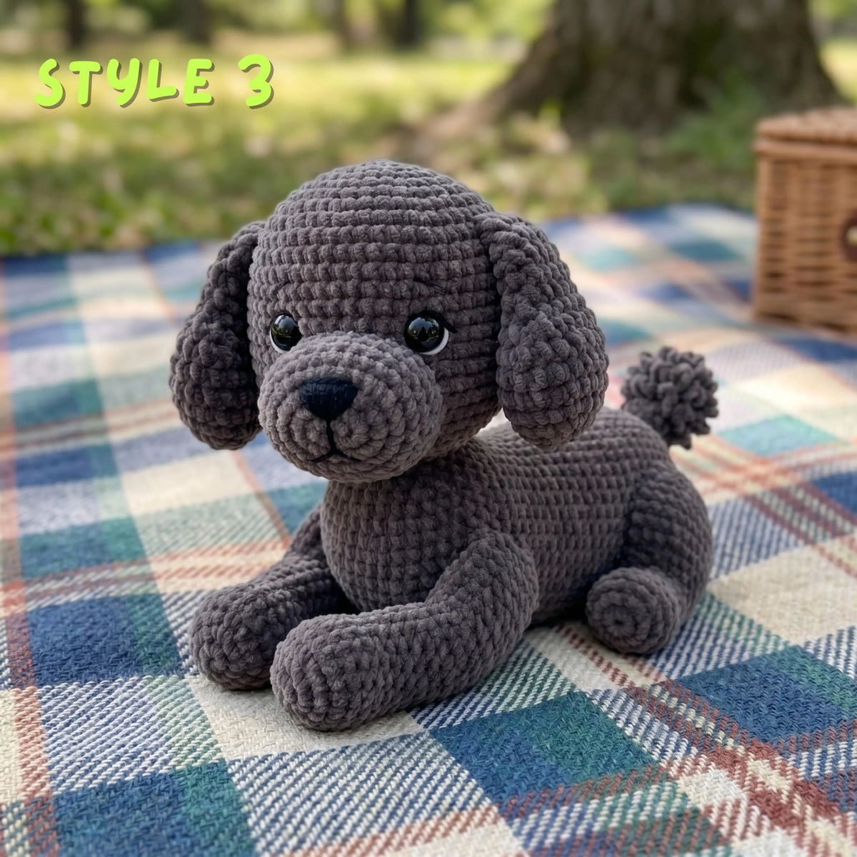 A crocheted plush puppy toy in dark gray sits on a blue, green, and white plaid blanket outdoors, with blurred trees in the background and the text 'STYLE 3' in the top left corner.