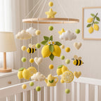 A baby crib mobile with a lemon and cloud theme, featuring felt lemon slices, whole and halved lemons, white clouds, yellow stars, bumblebees, and a small yellow teapot, hanging in a softly lit nursery.