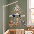Crocheted baby mobile with a crescent moon, clouds, stars, lion, giraffe, and elephant hanging from a wooden bar on a white crib stand, set in a nursery with a green wall and window.