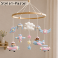 Pastel felt baby mobile hanging from a wooden hoop, featuring airplanes, stars, a cloud, and aviator hats with small child characters, shown in a softly lit nursery setting.