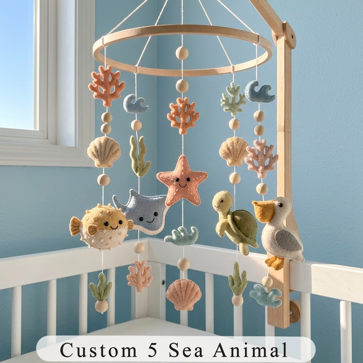 A wooden baby crib mobile with hanging sea-themed felt animals, including a starfish, turtle, fish, whale, and bird, shown in a crib against a blue wall. Text at the bottom reads 'Custom 5 Sea Animal'.