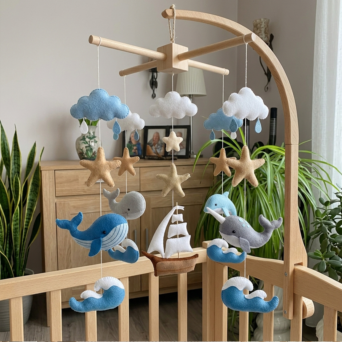 A wooden baby crib mobile with soft felt whale, cloud, starfish, and a small sailboat hanging in a nursery setting.